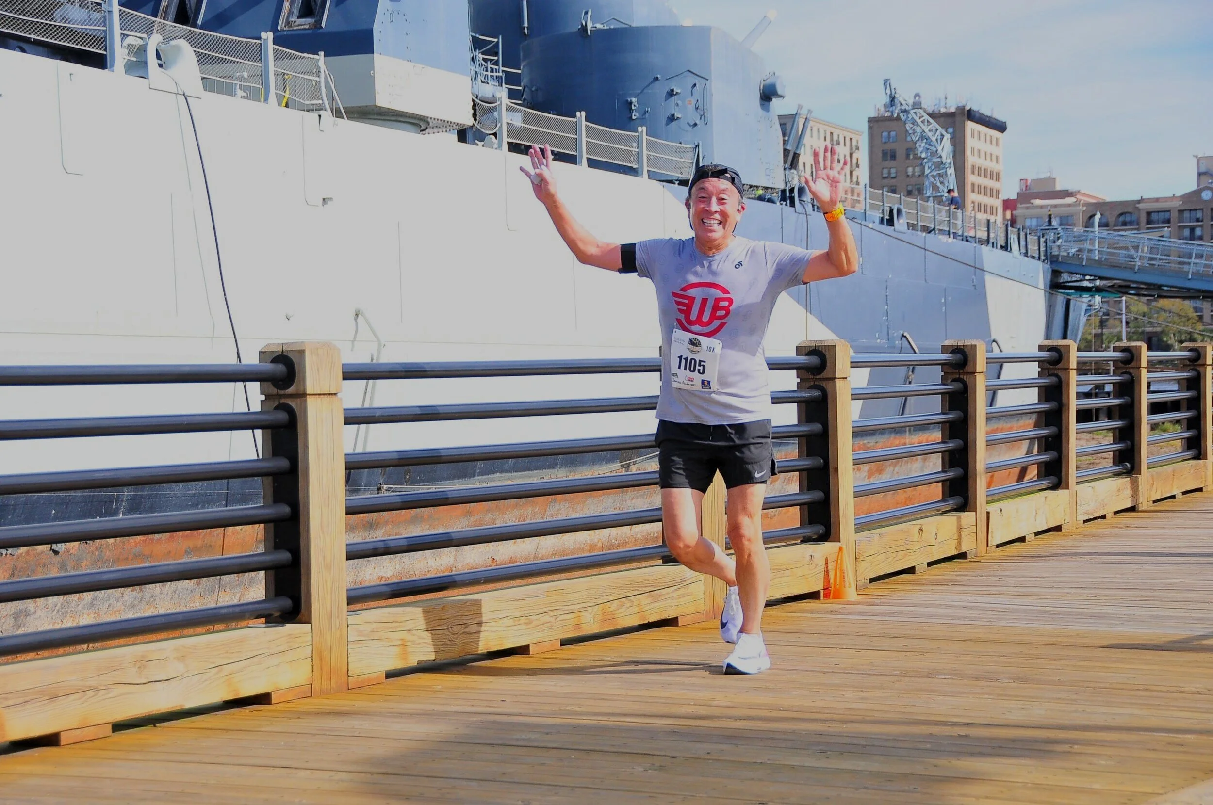 James celebrating with arms raised at a 10K finish on the boardwalk