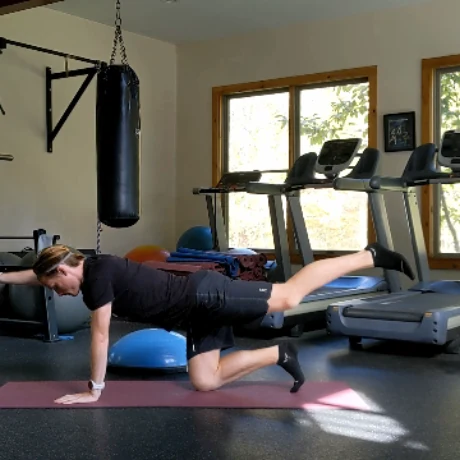 A runner holding a bird-dog position on a mat in a home gym, opposite arm and leg extended