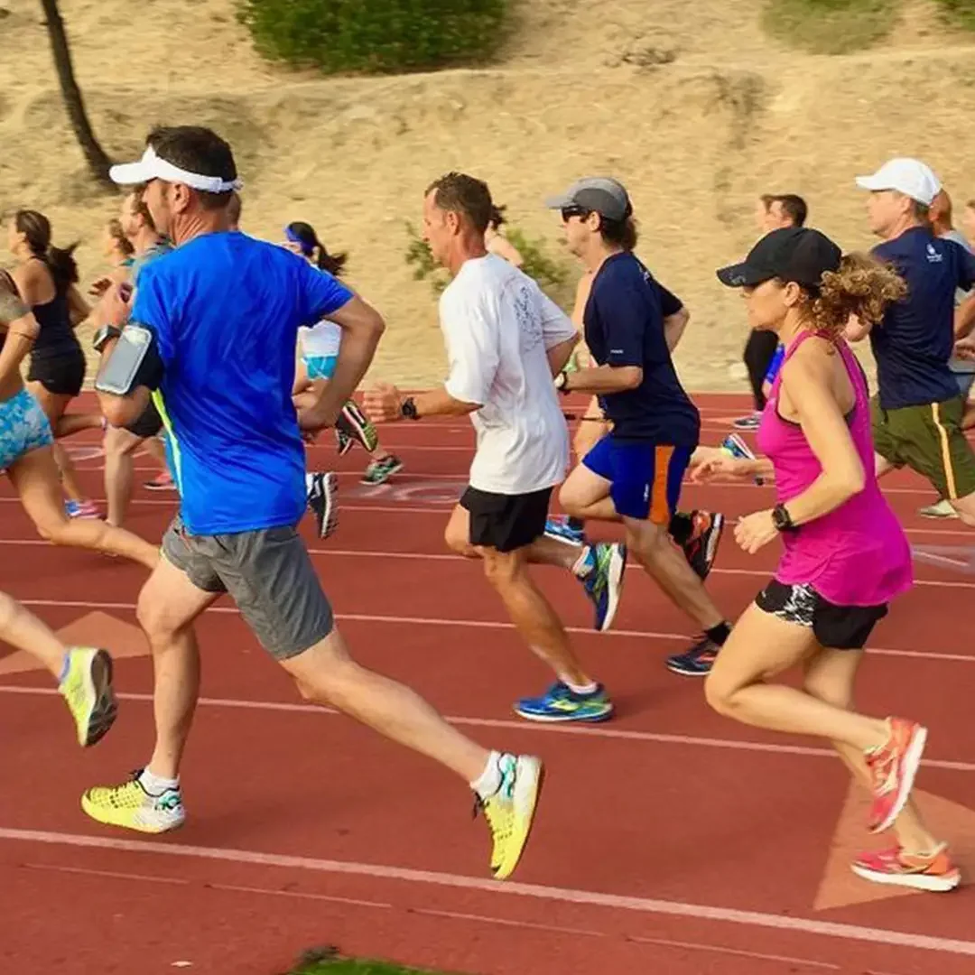 A solo runner on an outdoor track at sunrise, long shadow, empty lanes stretching ahead.