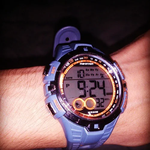 A handwritten pace band on a runner's wrist mid-race, mile splits in marker.