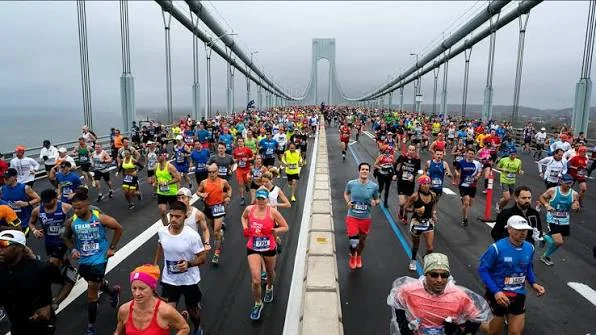 A lone marathoner seen from behind crossing a long bridge at dusk.