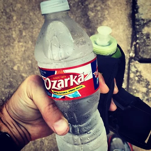 A trail runner in a hydration vest refilling a soft flask at a trailhead spigot.