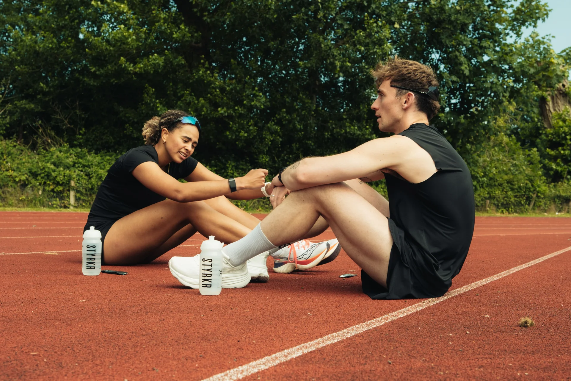 A runner catching breath between intervals, hands on knees, empty rubberized track behind them in warm evening light.