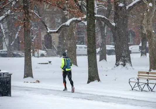 A runner in warm layers walking a foggy winter path at low sun, breath visible in cold air.