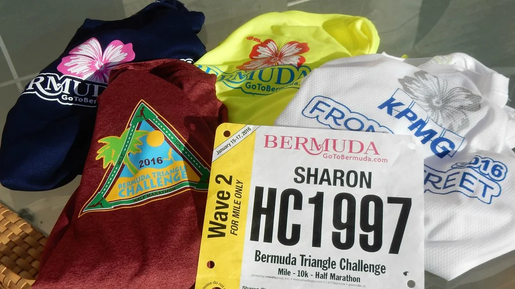 A handwritten pace band wristlet with mile splits in black marker beside a race bib on a wooden table.
