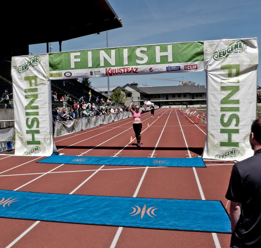 An empty country-road finish chute at golden hour with a banner overhead and small orange flags lining the lanes.