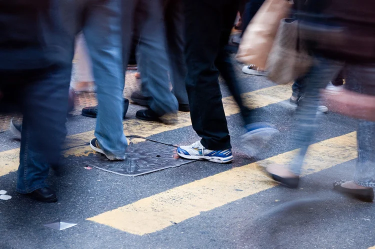 Long-exposure motion blur of legs walking across an urban crosswalk at dusk.