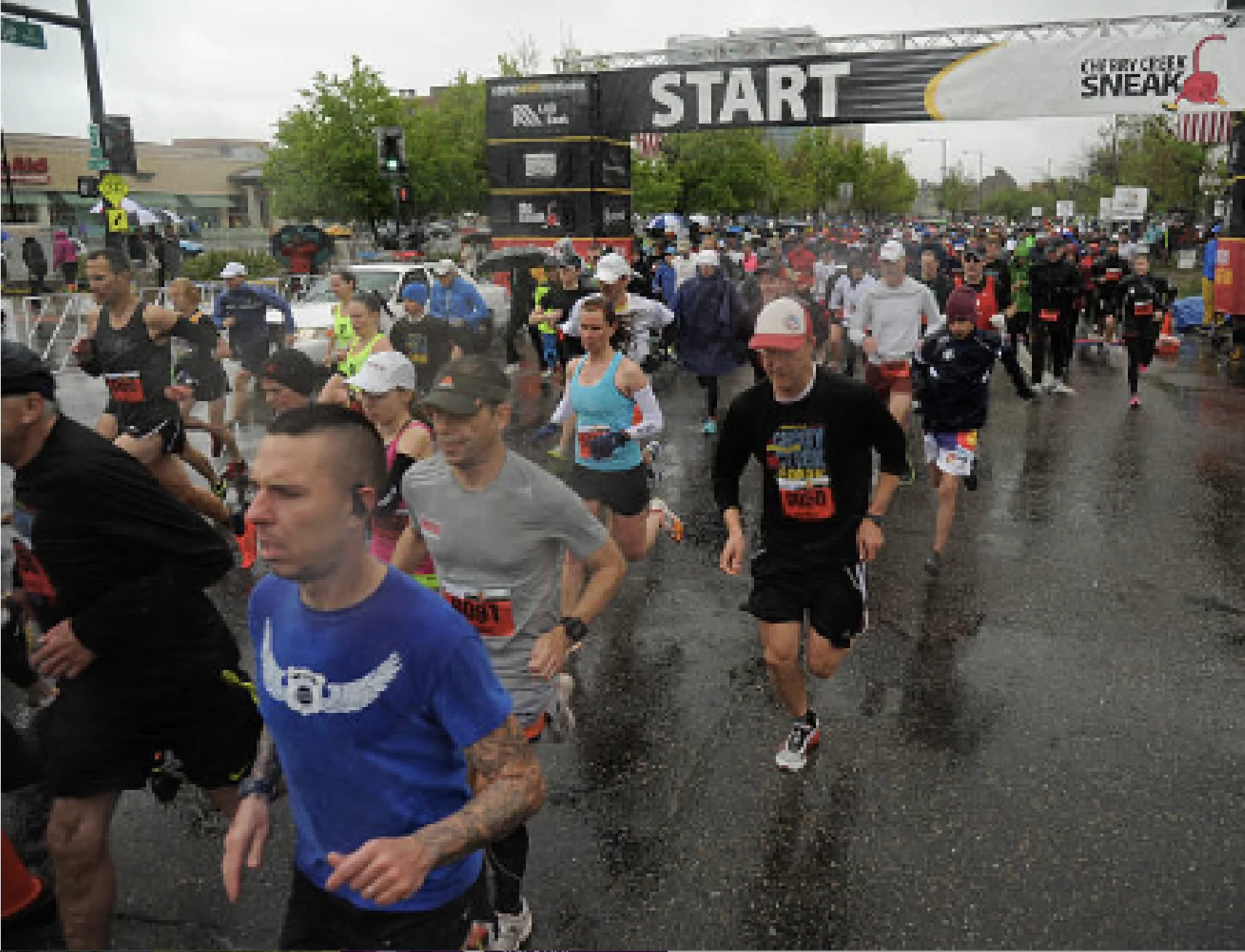Runners crossing the start line of the Cherry Creek Sneak 5K in Denver on a rainy race day.