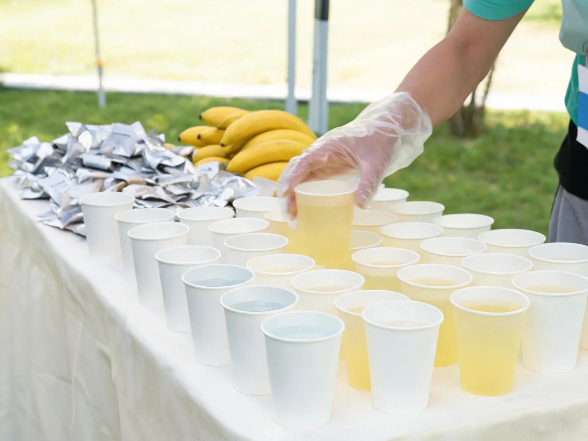 Volunteers' hands lining up paper cups on an aid station table before runners arrive.