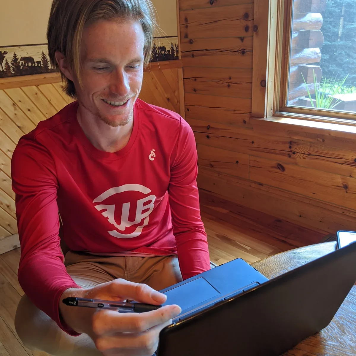 A laptop open to a weekly training calendar beside a marked-up paper notebook on a desk.