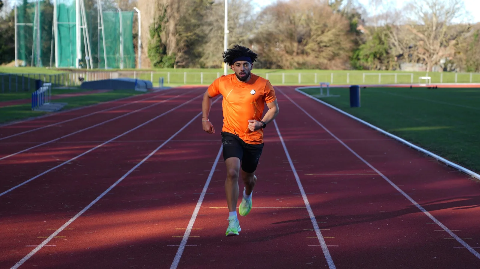 A runner in orange sprinting down a red outdoor track during an interval session.