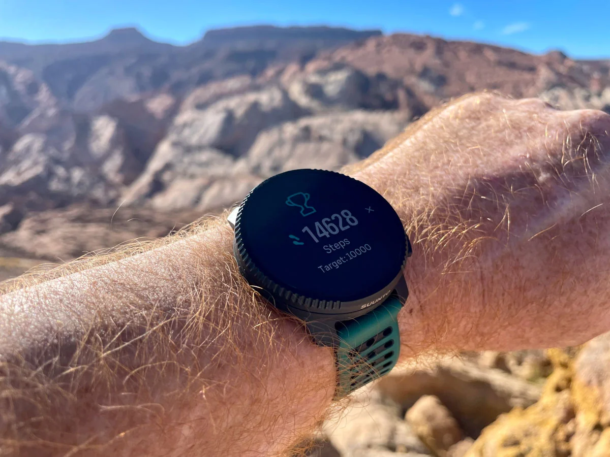 A GPS watch on a wrist next to a water bottle on a park bench, mid-run break.