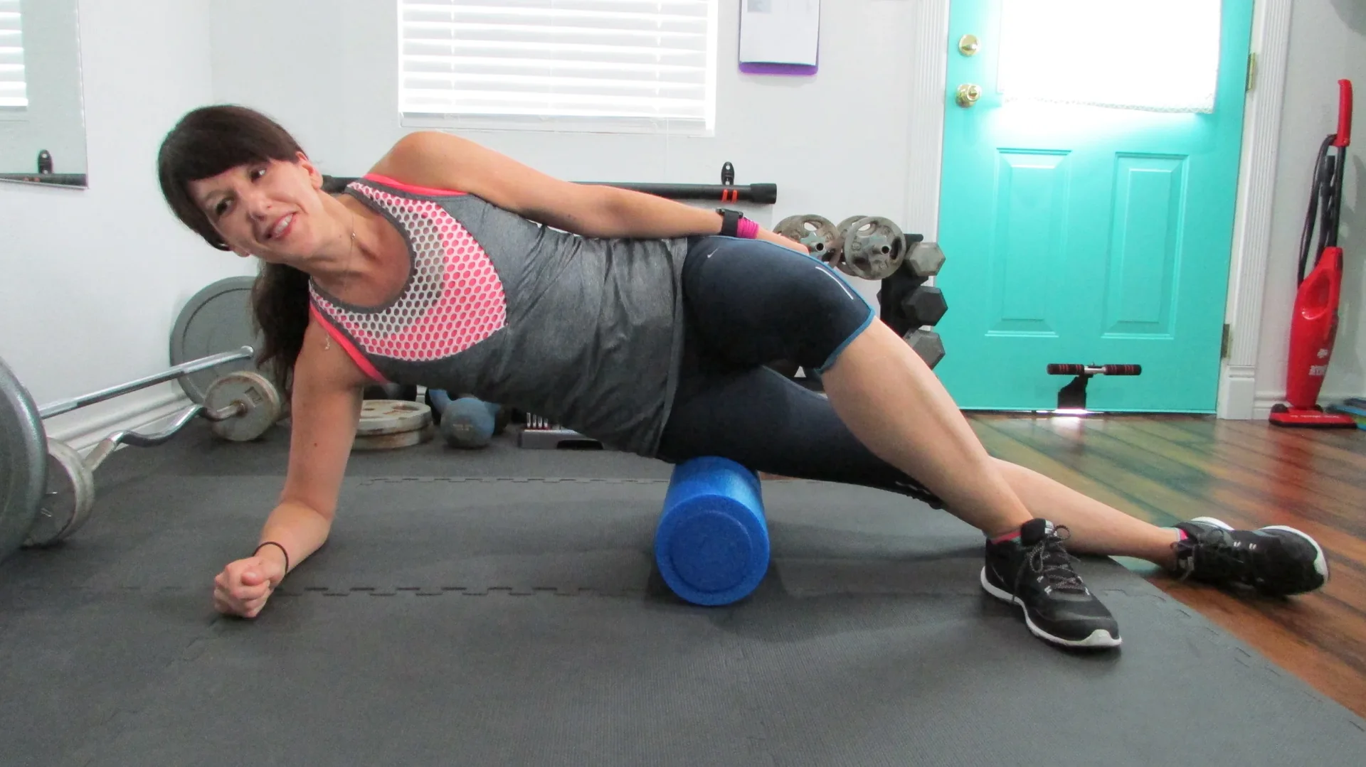 A runner foam rolling the outer thigh on a living room floor in evening lamp light.