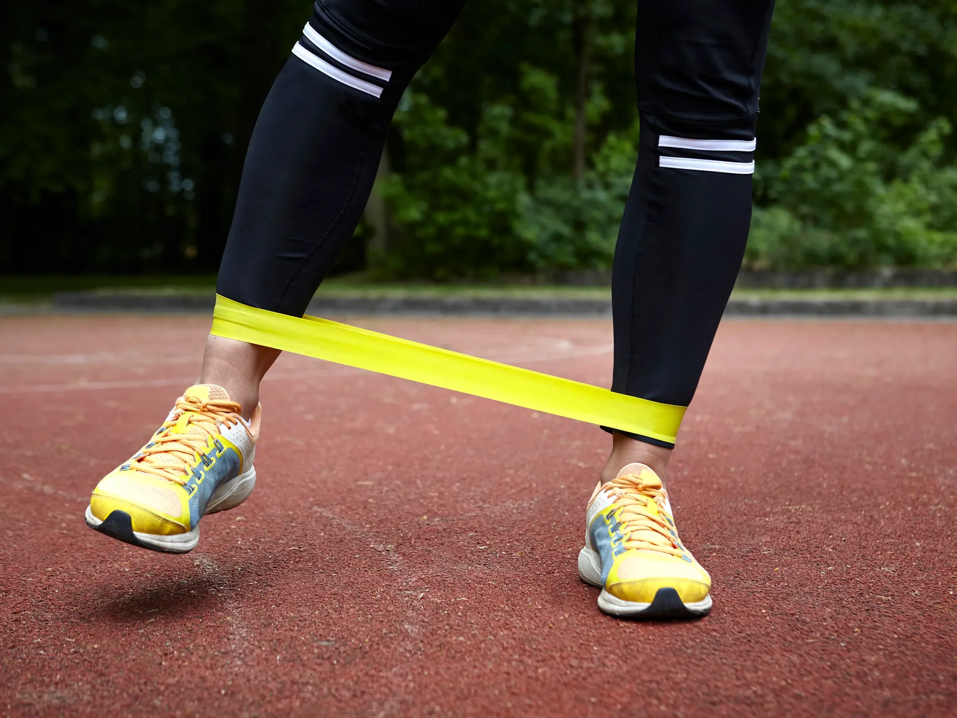 A resistance mini-band stretched around a runner's ankles mid lateral-walk rep.