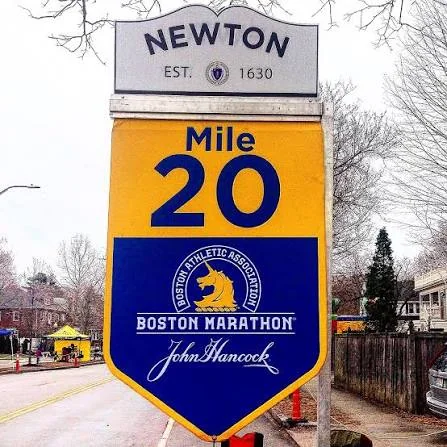 A painted mile-20 marker on an open marathon course road in low morning sun with long shadows across asphalt.