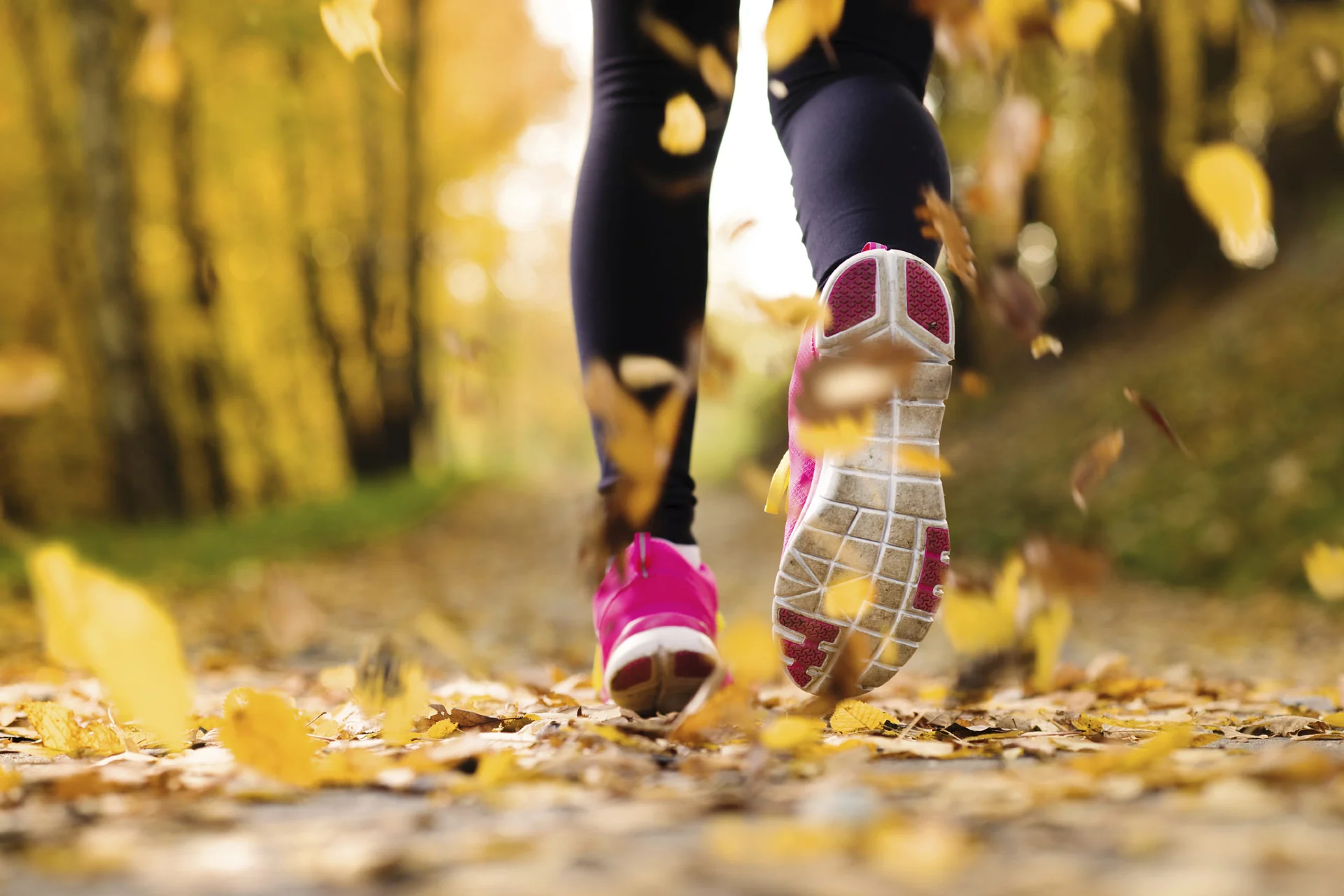 A runner on an easy recovery jog through wet fall leaves in a park under gray drizzle.