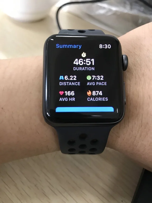 A GPS running watch resting on weathered asphalt showing 6.20 miles at the finish of a 10K.