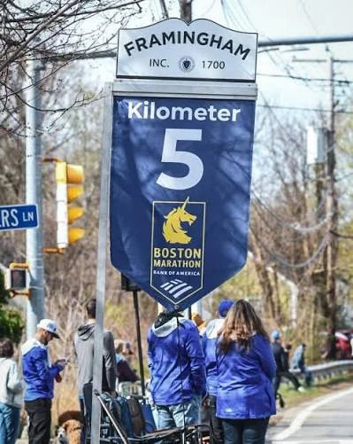 A concrete European road-race kilometer marker post beside a metal barricade on a city course.
