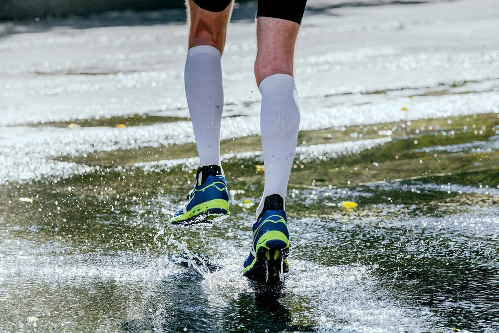 Close-up of knee-high compression socks and new shoes stepping onto wet grass after rain.