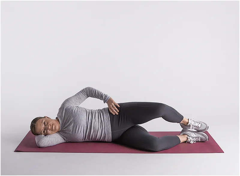 Bare feet performing a side-lying hip strengthening exercise on a wooden floor in warm morning light.