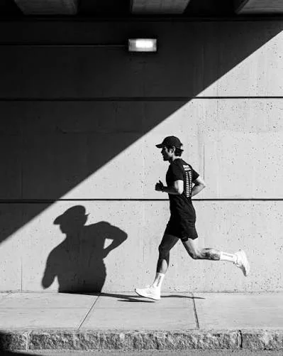 A quiet neighborhood sidewalk in early morning light with a single runner's long shadow on the pavement.