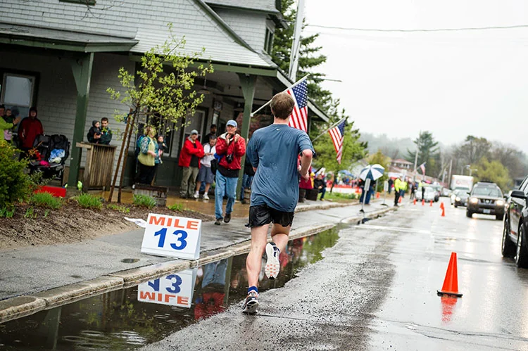 A mile 10 marker sign on a riverside half marathon course with runners passing in light rain.