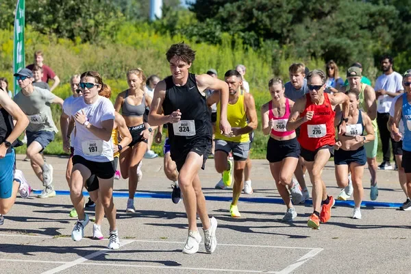 A runner's long shadow stretched across warm sunlit pavement, only the shoes visible at the top edge of the frame.