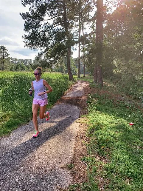 A solo runner mid-stride on a quiet paved road at mid-morning, arms relaxed, controlled effort.