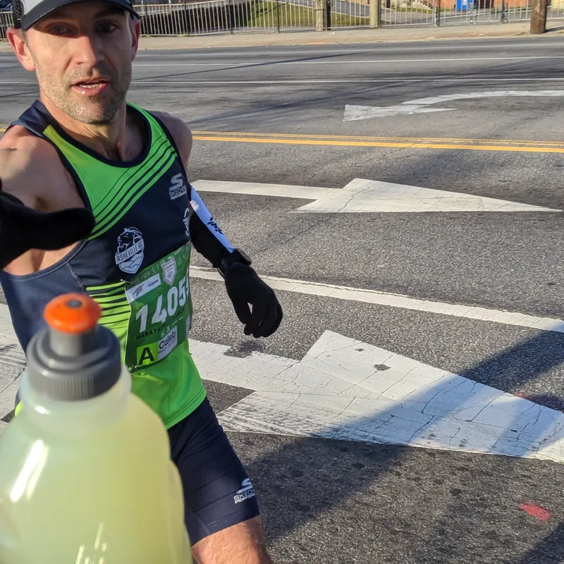 A marathon runner reaching for a handheld bottle of sports drink handed to him mid-race